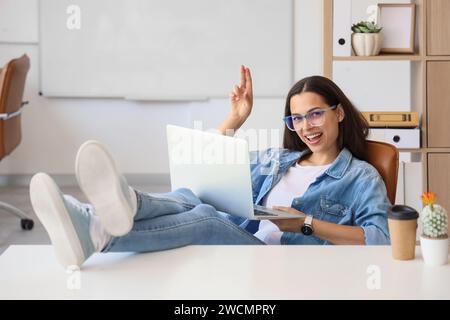 Bella giovane programmatore donna con le gambe sul tavolo che riposano in ufficio Foto Stock