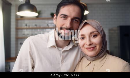 Ritratto di una giovane felice coppia sposata che si abbraccia in cucina, sorride e guarda la fotocamera Foto Stock