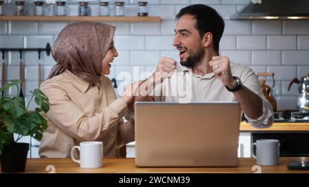 Giovani sposati coppia felice uso portatile leggere notizie online ricevuto un grande messaggio di posta elettronica urlare con gioia festeggiando opportunità a casa in cucina Foto Stock