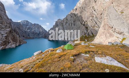 Tenda verde presso un lago di montagna blu tra ripide vette rocciose, il lago Kol Suu, i monti Sary Beles, la provincia di Naryn, il Kirghizistan Foto Stock