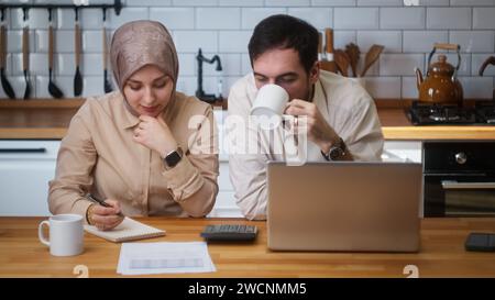 Una coppia seduta in cucina con notebook paga le bollette, usa la calcolatrice per contare le spese, gestisci le finanze, controlla il budget, senti stressato Foto Stock