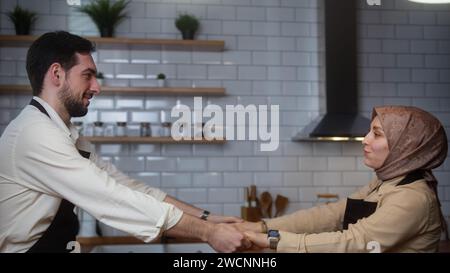 Felice coppia sposata che indossa grembiuli che si diverte a ballare mentre cucina la cena insieme, trascorrendo del tempo in cucina moderna Foto Stock