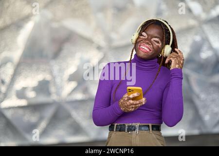 Donna vivace e gioiosa con smartphone e cuffie Foto Stock