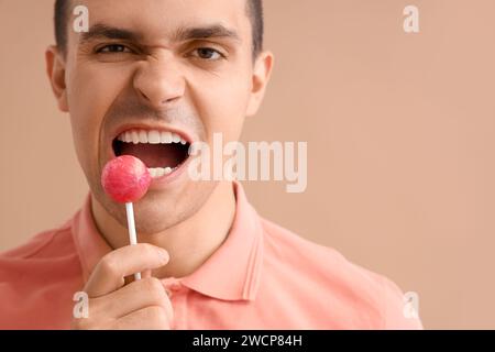 Bellissimo giovane con lecca lecca su sfondo marrone. Concetto di odontoiatria Foto Stock