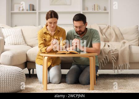 Coppia di famiglie che pregano per la Bibbia insieme a un tavolo al chiuso Foto Stock