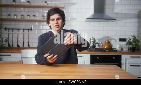 Un giovane uomo uscito che gioca a un videogame su un tablet mentre è seduto in cucina a casa. Eccitato concentrato maschile coinvolto in un gioco interessante Foto Stock