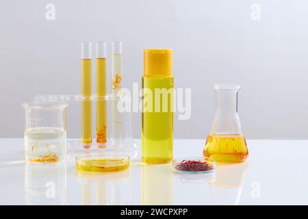 Flacone senza marchio riempito con liquido e disposto con vetreria da laboratorio su sfondo bianco. Lo zafferano è la spezia più costosa del mondo Foto Stock