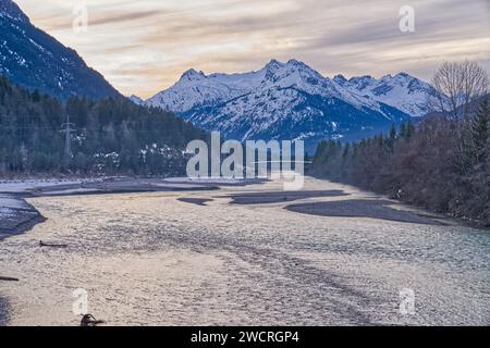 Un fiume sereno che scorre attraverso una lussureggiante foresta circondata da maestose montagne coperte di neve Foto Stock