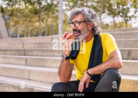 l'uomo anziano riposa mangiando una mela dopo l'allenamento Foto Stock
