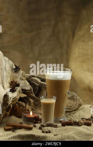Caffè di vetro con un bicchiere di liquore irlandese e spezie. Sfondo tessuto con spazio di copia Foto Stock