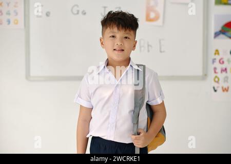 Ritratto di un ragazzino sorridente con zaino in classe Foto Stock