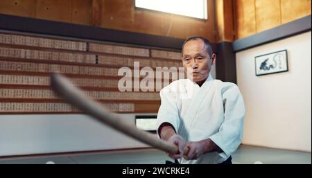 Spada Aikido, arti marziali e attacco uomo maturo per addestramento, autodifesa o tecnica di combattimento. Dojo, giapponese ed esperto con armi di legno Foto Stock