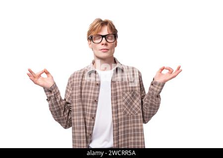 un giovane caucasico dai capelli rossi in una camicia sopra una t-shirt medita con gli occhi chiusi Foto Stock