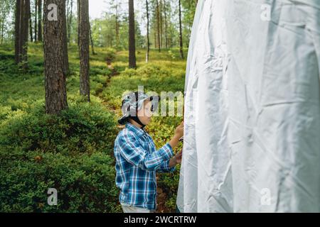 carino piccolo ragazzo caucasico che mette una tenda. Concezione di campeggio per famiglie, ombre del tramonto dagli alberi. Campeggio per famiglie. Foto di alta qualità Foto Stock