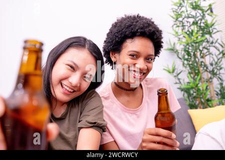 Due giovani donne sorridono e tengono in mano le bottiglie di birra, trascorrendo momenti di relax insieme in un'atmosfera casalinga Foto Stock