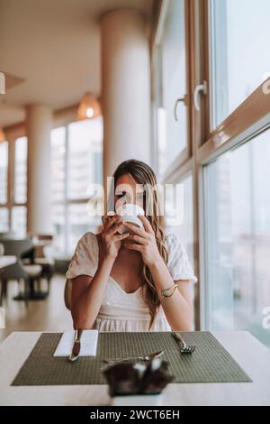 Una donna attraente che si gode un momento vicino alla finestra, assaporando una tazza di caffè appena fatto Foto Stock