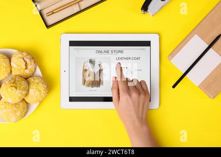 Donna con un tablet che fa acquisti online su sfondo giallo, vista dall'alto Foto Stock