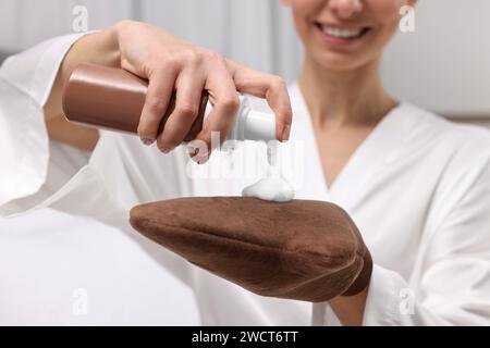 Autoabbronzante. Donna che applica il prodotto cosmetico sul guanto abbronzante in interni, primo piano Foto Stock