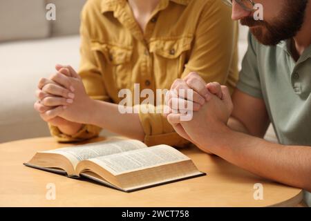 Coppia di famiglie che pregano per la Bibbia insieme a un tavolo al chiuso, primo piano Foto Stock