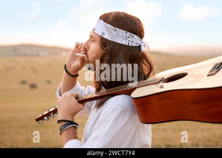 Elegante uomo hippie con fumante chitarra in campo Foto Stock