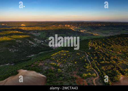 Il crepuscolo bagna il paesaggio di Alcarria in sfumature dorate mentre la luna si innalza su colline ondulate punteggiate da vegetazione lussureggiante e campi coltivati Foto Stock