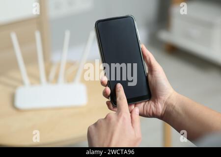 Donna con smartphone che si connette a Internet tramite router Wi-Fi in interni, primo piano Foto Stock