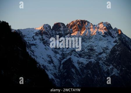 Le cime innevate delle montagne si crogiolano nel caldo bagliore del sole che tramonta con ombre contrastanti Foto Stock