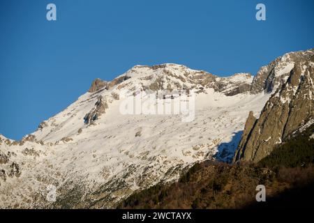 L'immagine mostra una splendida cima innevata della montagna, bagnata dalla luce del sole, con un cielo blu scuro sullo sfondo Foto Stock