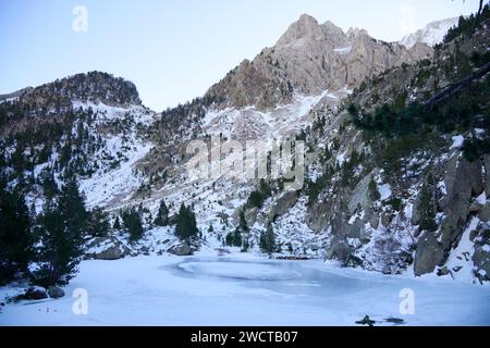 Un tranquillo lago ghiacciato sullo sfondo di aspre montagne innevate, con alberi che emergono dalle piste innevate Foto Stock