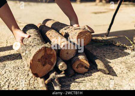 Vista ravvicinata delle mani che collocano tronchi appena tagliati su una superficie in calcestruzzo, evidenziando il lavoro manuale all'aperto Foto Stock