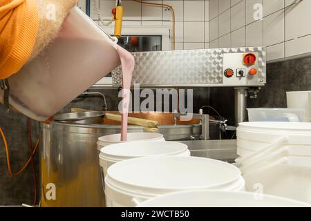 Un caseificio versa latte fresco e cremoso in una grande vasca di acciaio per la cagliatura del primo passo del processo di produzione del formaggio in una cucina professionale Foto Stock