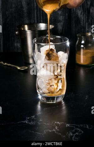 Il processo di preparazione di una frappe greca viene catturato qui, con ghiaccio e caffè istantaneo in un bicchiere, conditi con una miscela di caffè cremoso, promettendo una re Foto Stock