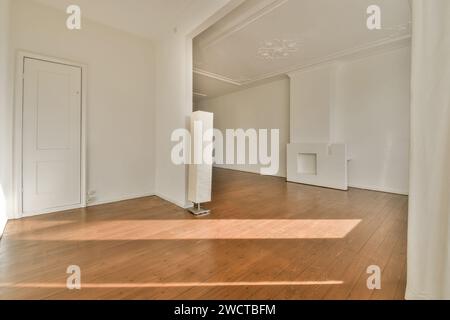 Una camera vuota con pavimenti in legno duro, pareti bianche e una grande finestra che getta luce solare nello spazio, caratterizzata da dettagli minimalisti. Foto Stock