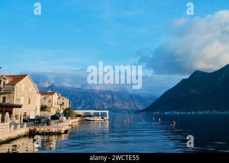 Antiche case in pietra sulla riva di Perast sullo sfondo delle montagne al sole. Montenegro Foto Stock