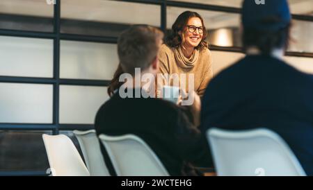 In un ufficio luminoso, un gruppo eterogeneo di colleghi si impegna in una discussione dinamica. Una donna sicura guida il team, presentando idee a un autobus attento Foto Stock