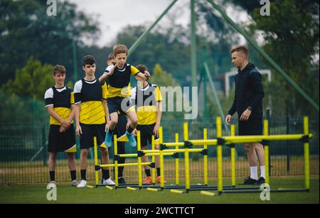 Adolescenti al campo di allenamento di calcio. Ragazzi in allenamento di calcio con un giovane allenatore. Gli atleti di livello Junior saltano sugli ostacoli e migliorano la forza e la forza Foto Stock