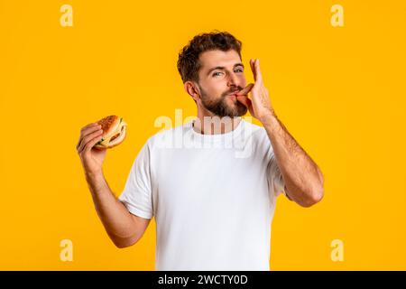 Ritratto di un uomo affamato sorridente che mangia Burger Licking Fingers, Studio Foto Stock