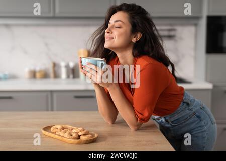 Soddisfatta giovane donna che assaggia il caffè a casa Foto Stock