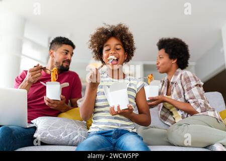 Felice famiglia africana che mangia in salotto e si diverte a trascorrere del tempo insieme. Piatti da asporto casalinghi Foto Stock