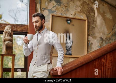 leader aziendale concentrato e attraente con barba dallo stile elegante e bevendo il suo caffè Foto Stock