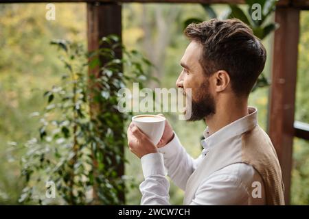 leader aziendale allegro e attraente, con barba dallo stile elegante e bevendo il suo caffè Foto Stock