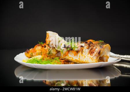 pesce cotto in forno con spezie e verdure in un piatto isolato su sfondo nero. Foto Stock