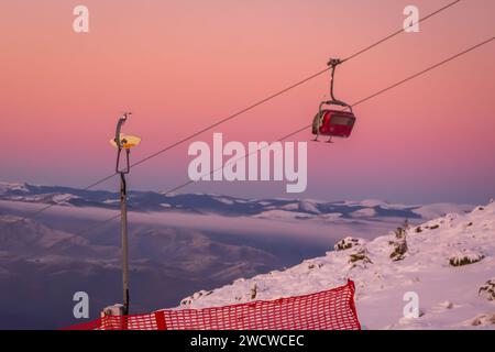 Uno splendido paesaggio invernale caratterizzato da una maestosa montagna innevata, adornata da un vivace impianto di risalita rosso che trasporta gli appassionati di sci e le nevi. Foto Stock