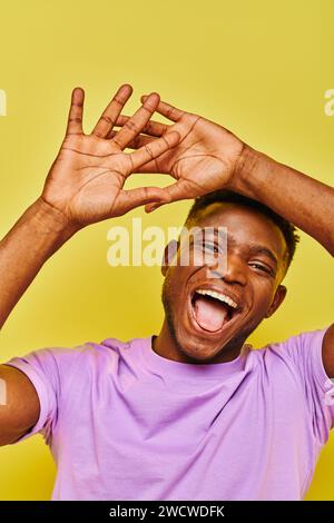 allegro e divertente uomo afro-americano che gestiva e si stendeva la lingua su sfondo giallo Foto Stock