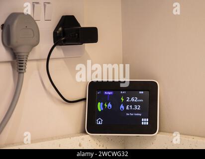 Display remoto con contatore intelligente che mostra l'elettricità e il gas utilizzati fino a quel momento quel giorno in kwh e sterline britanniche con la presa elettrica a muro in stile britannico sopra Foto Stock