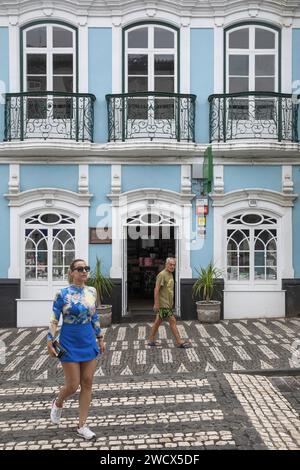 Portogallo, arcipelago delle Azzorre, isola di Terceira, Angra do Heroismo, giovane donna che attraversa una strada con ciottoli bianchi e neri di fronte a una c Foto Stock