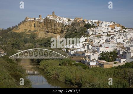 Spagna, Andalusia, Arcos de la Frontera, case bianche che scendono da uno sperone roccioso e scendono verso il fiume Guadelete y Majaceite con sponde verdi e attraversate da un ponte di metallo Foto Stock