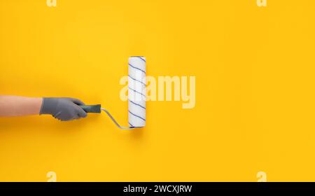 Donna mano in guanto che tiene un rullo di vernice su sfondo giallo. Foto Stock