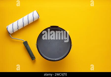 Aprire la lattina di vernice grigia con un rullo su sfondo giallo. Concetto di ristrutturazione della casa. Foto Stock