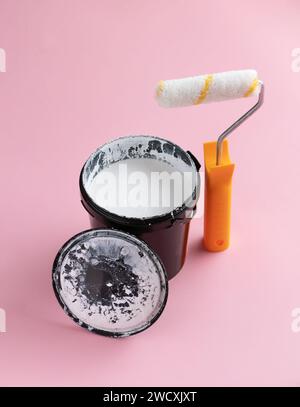 Barattolo di vernice bianca e rullo su sfondo rosa. Concetto creativo di ristrutturazione della casa. Foto Stock